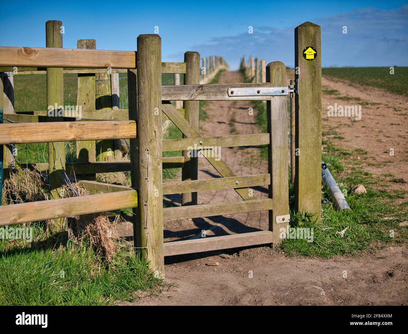 Una porta di bacia in legno dà accesso ad un percorso lungo il bordo di un campo. Preso in un'area rurale nel nord-ovest dell'Inghilterra nel Regno Unito in una giornata soleggiata in Foto Stock