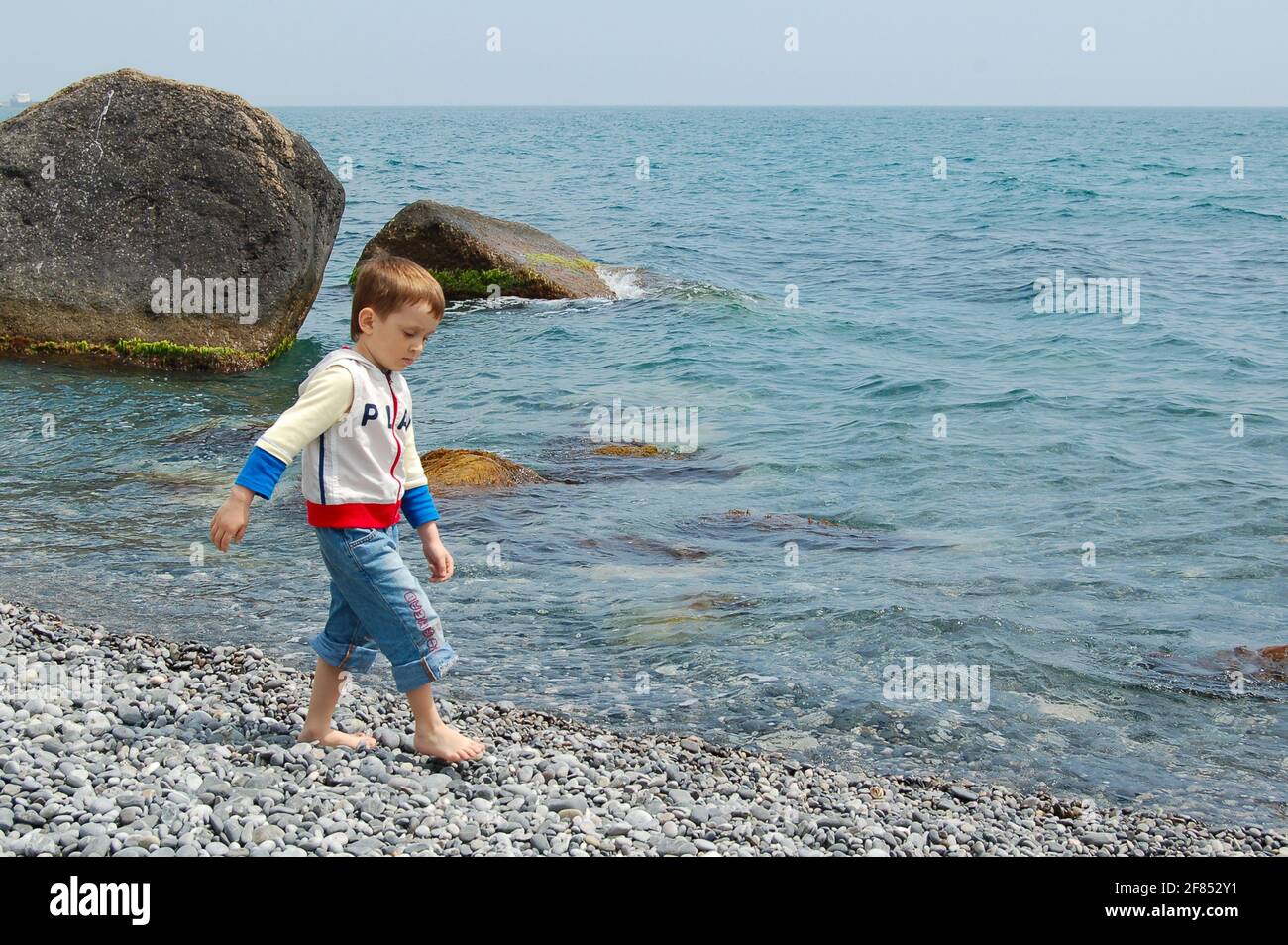 Yalta, Ucraina - 03.05.2009: Un ragazzo corre lungo la riva del mare. I bambini amano giocare con le rocce sulla spiaggia di ciottoli. Foto Stock