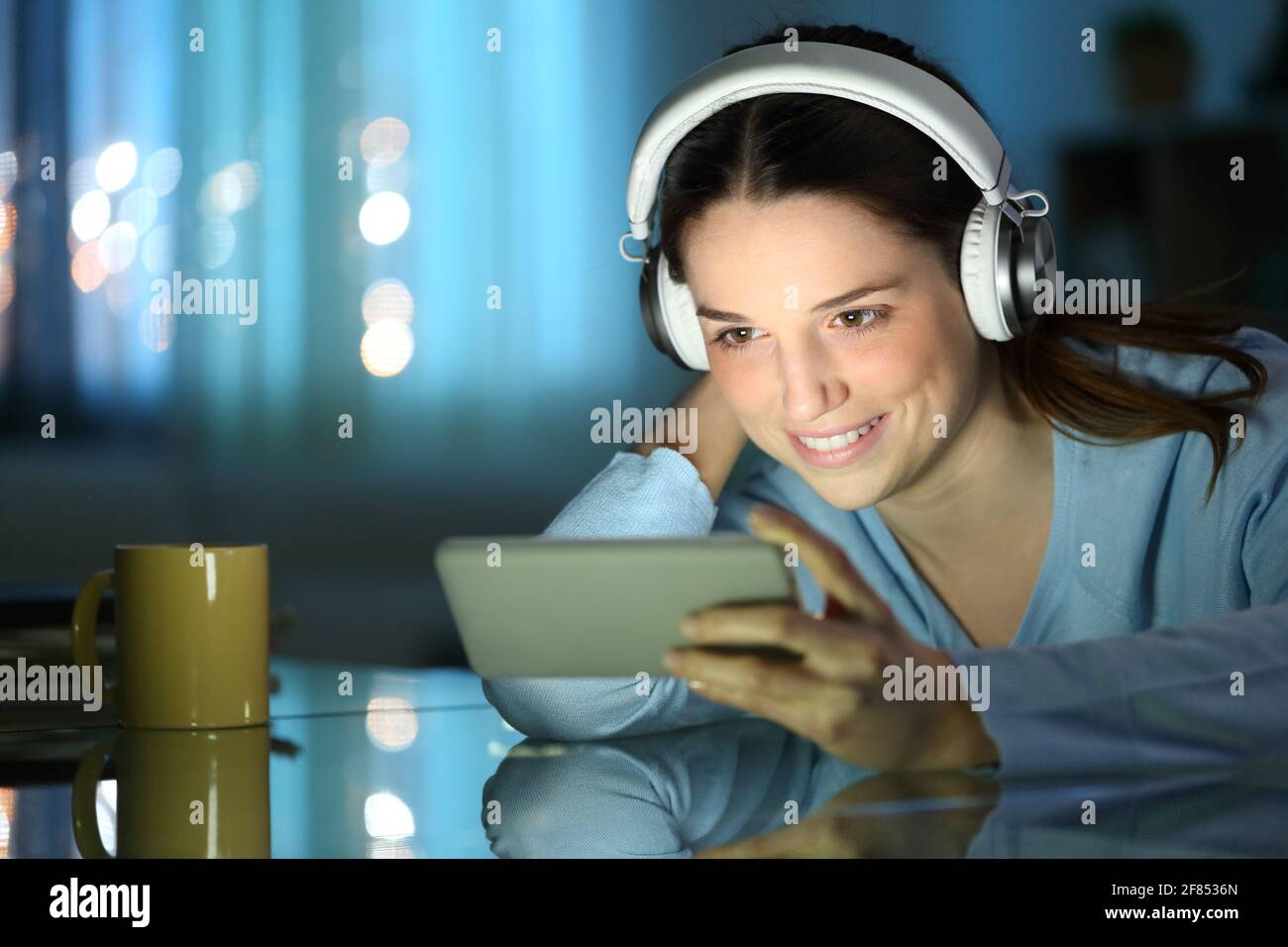 Donna felice che guarda i video online sullo smartphone di notte a casa Foto Stock
