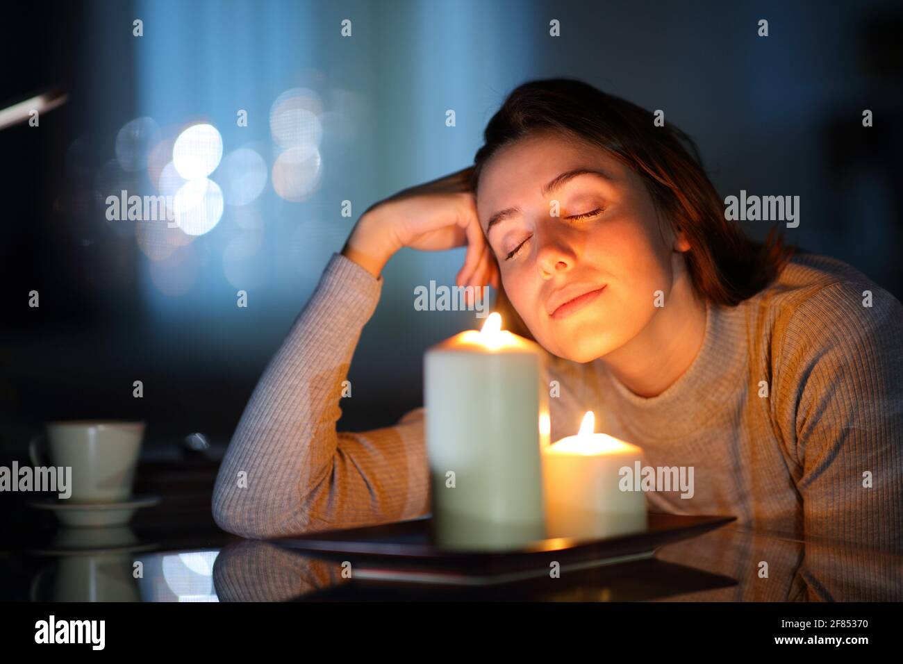 Donna rilassata che odora candele aromatiche nella notte in soggiorno a casa Foto Stock