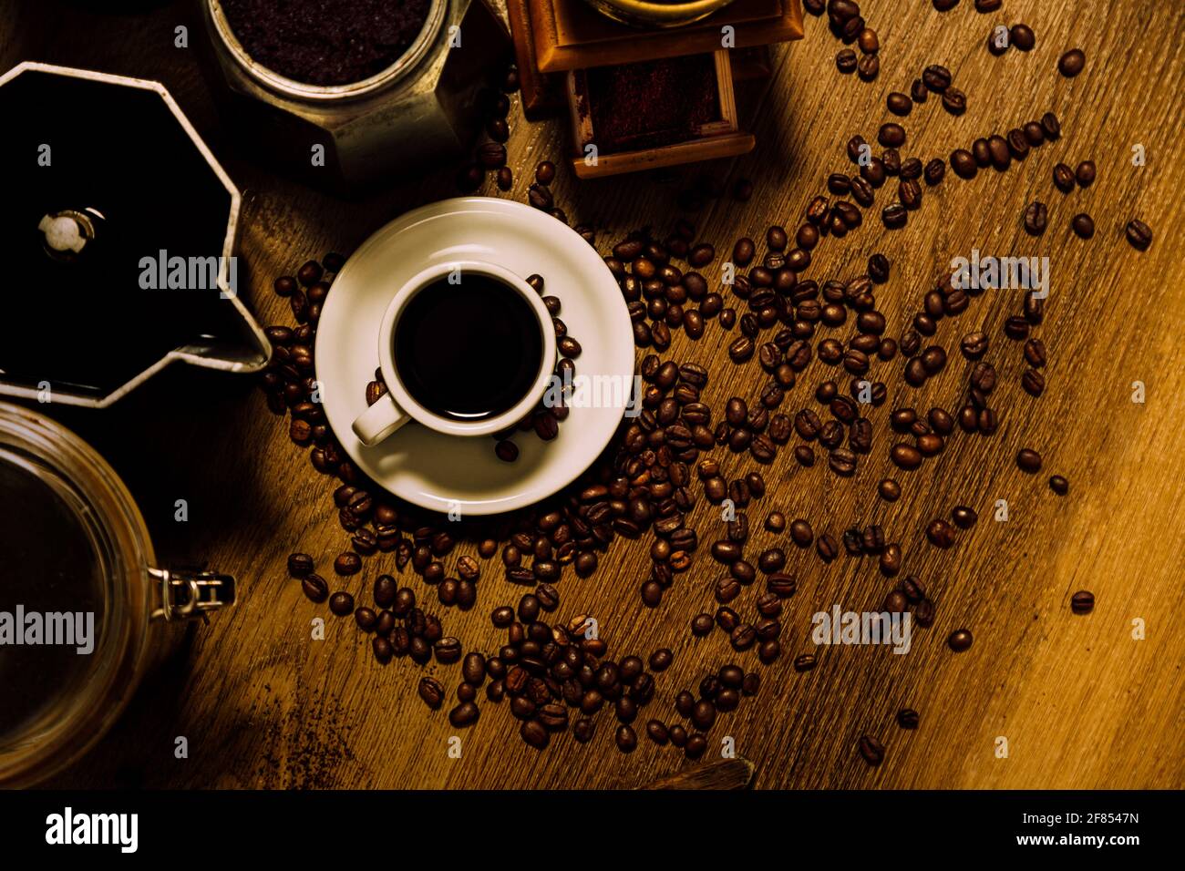 Roba di caffè. Vista dall'alto di una tazza bianca con caffè nero, moka italiana, un mulino e cereali su un tavolo di legno. Stile rustico vintage. Foto Stock