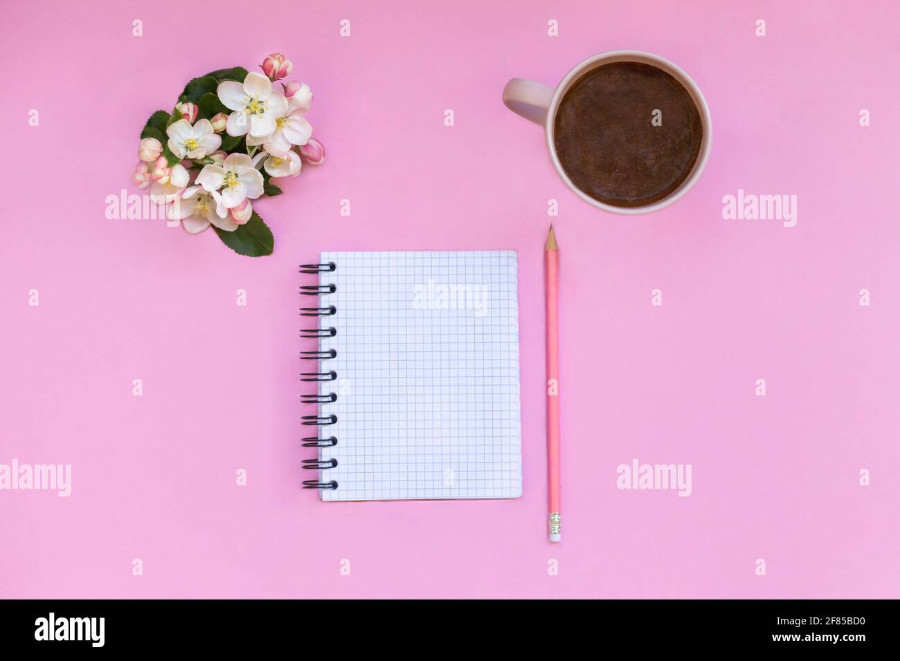 Un quaderno per note giace su uno sfondo rosa, accanto a penna, caffè e fiori. Pianificazione personale del tempo e dei lavori Foto Stock