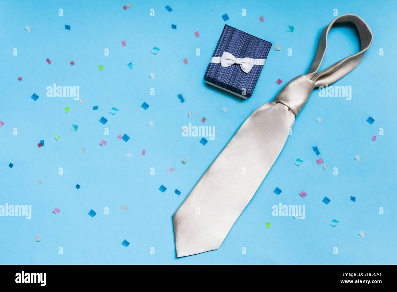 Confezione regalo blu con cravatta bianca, su sfondo blu con confetti colorati. Padre giorno concetto, congratulazioni ad un uomo, figlio, collega. Foto Stock