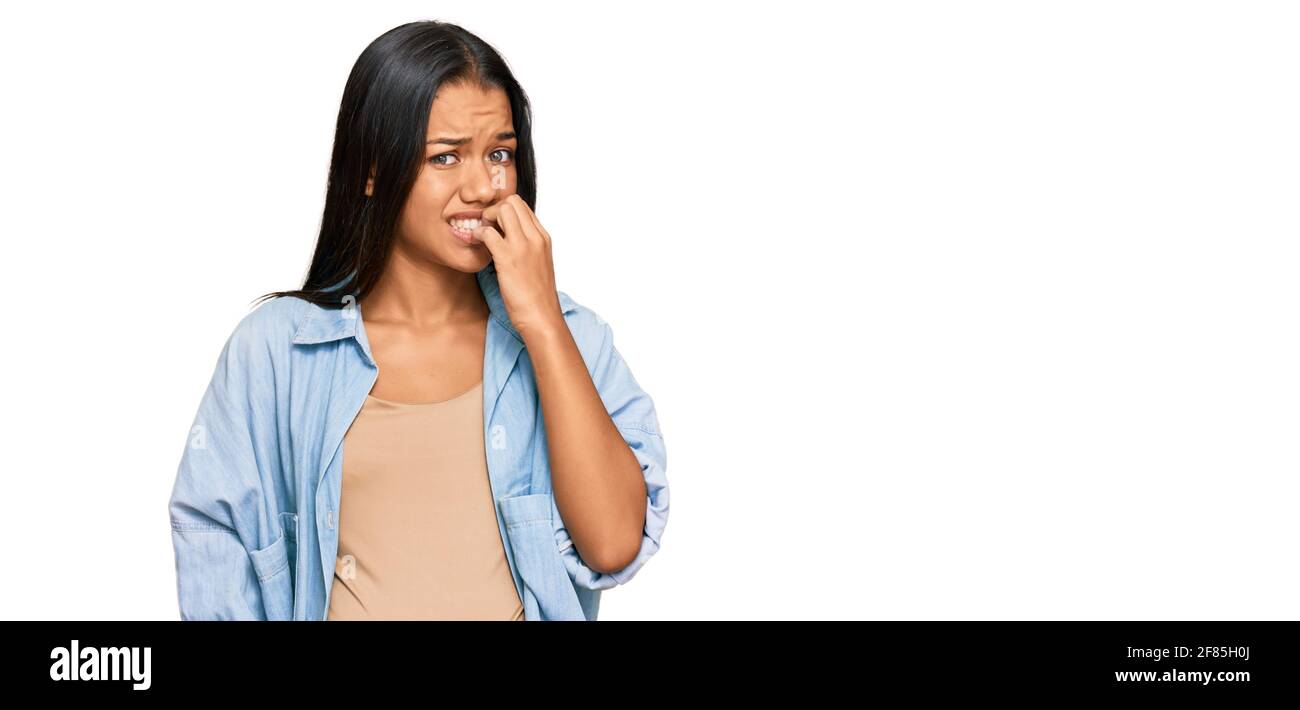 Bella donna ispanica che si aspetta un bambino che mostra la pancia incinta cercando stressato e nervoso con le mani sulla bocca che mordano unghie. Problema di ansia. Foto Stock