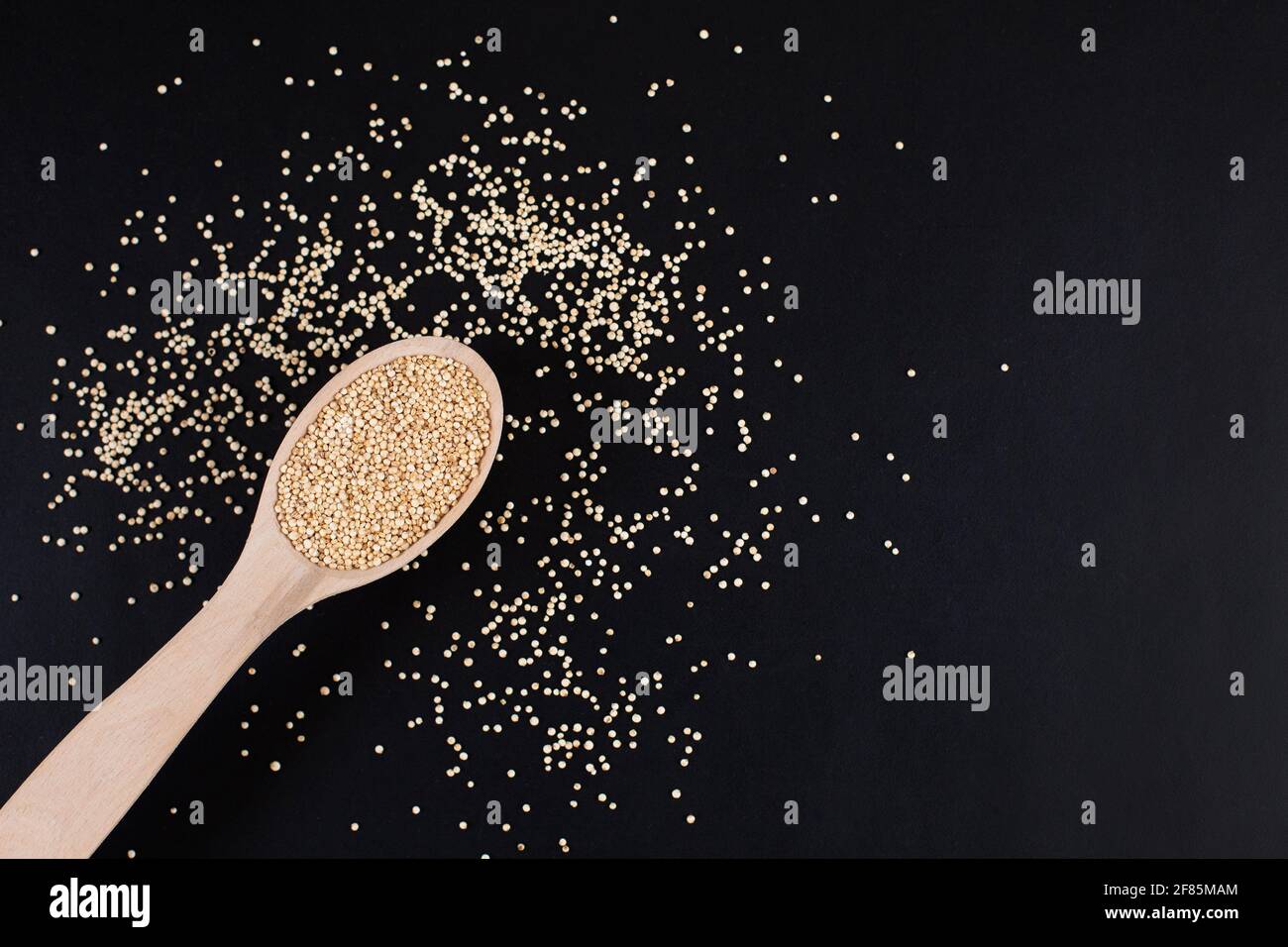 Grani bianchi di quinoa organici grezzi in cucchiaio di legno su fondo nero. Grano antico senza glutine. Dieta sana. Foto Stock