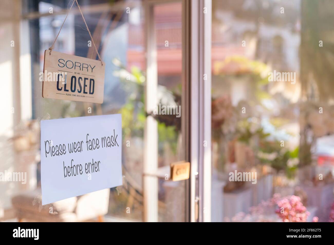 Siamo spiacenti siamo chiusi cartello legno e si prega di indossare la maschera per entrare in carta su porta di vetro protezione per pandemia di coronavirus. Chiudi negozio, ristorante Foto Stock