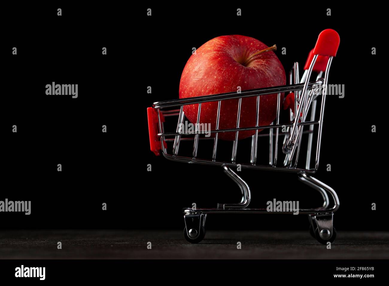 Immagine di sfondo scura con un carrello giocattolo pieno di Una mela rossa UN'immagine di concetto per l'acquisto più sano frutta e verdura nella drogheria o sup Foto Stock