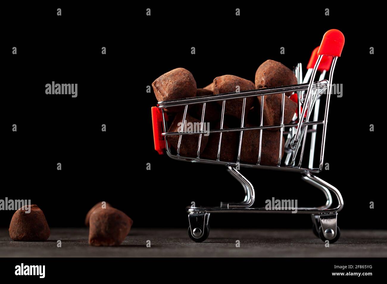 Immagine di sfondo scuro con un carrello giocattolo pieno di tartufi al cioccolato. Un'immagine concettuale per lo shopping natalizio, giorno di San Valentino dove il cioccolato Foto Stock