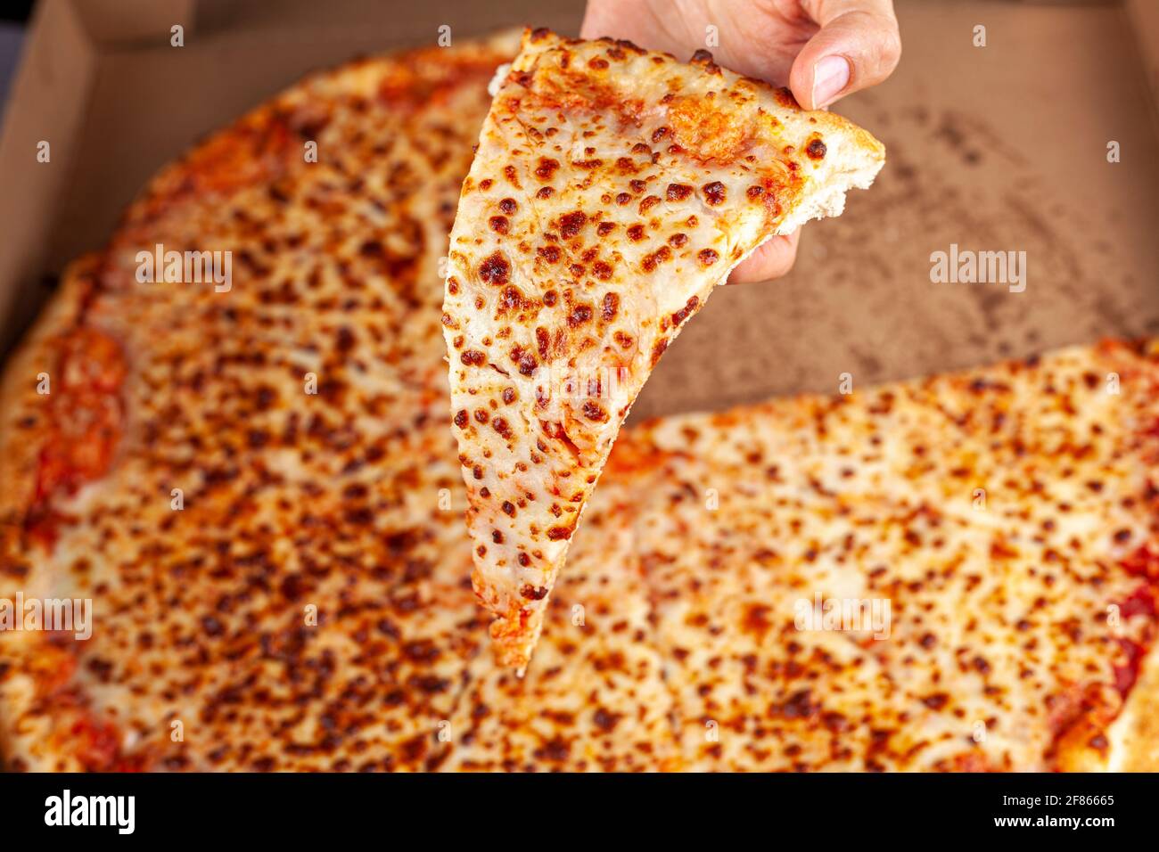 Primo piano immagine dall'alto di una donna caucasica che tiene una fetta di pizza al formaggio fresco con una grande pizza in cartiera sullo sfondo. Immagine concettuale per Foto Stock