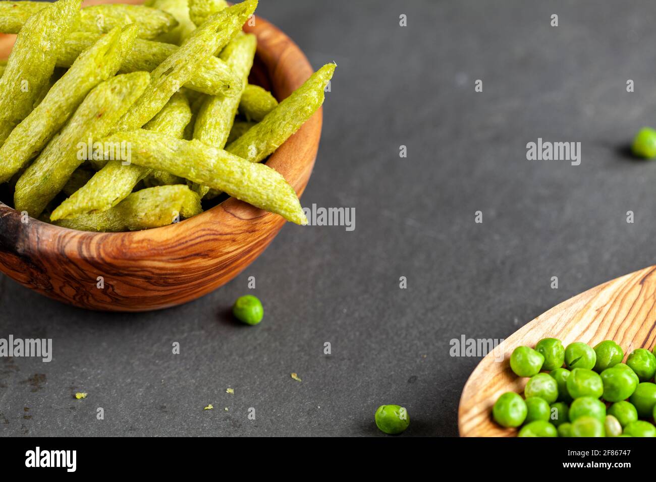 Closeup immagine isolata di una ciotola di legno riempita con croccante raccolto verde snacks piselli, un'alternativa più sana e nutriente alle patatine. Vie angolate Foto Stock