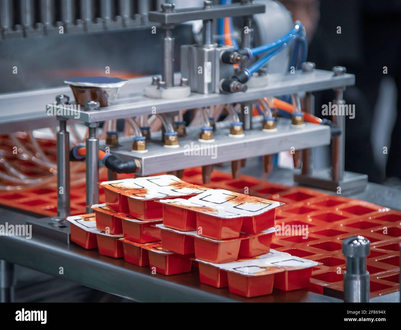Processo di riempimento e sigillatura automatico del bicchiere per salsa di ketchup. Industria alimentare Foto Stock