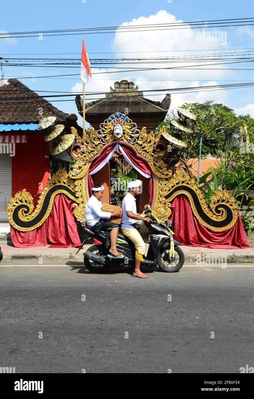 Padre e figlio balinese che prendono offerte di tempio su scooter therioter. Foto Stock