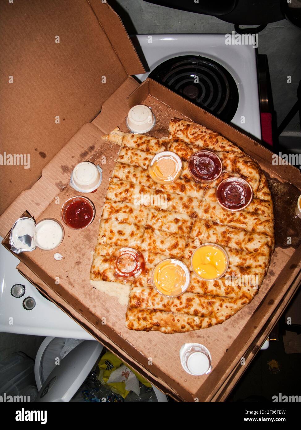 La vecchia pizza mangiata a metà ha lasciato sopra dopo una festa selvaggia in una casa disordinata, scattata in stile flash-on-camera. Foto Stock