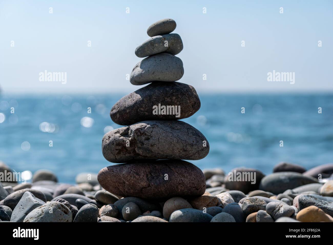 Equilibrata piramide di ciottoli sulla spiaggia in una giornata di sole. Abstract Sea bokeh sullo sfondo. Messa a fuoco selettiva. Pietre Zen sulla spiaggia di mare, meditazione Foto Stock