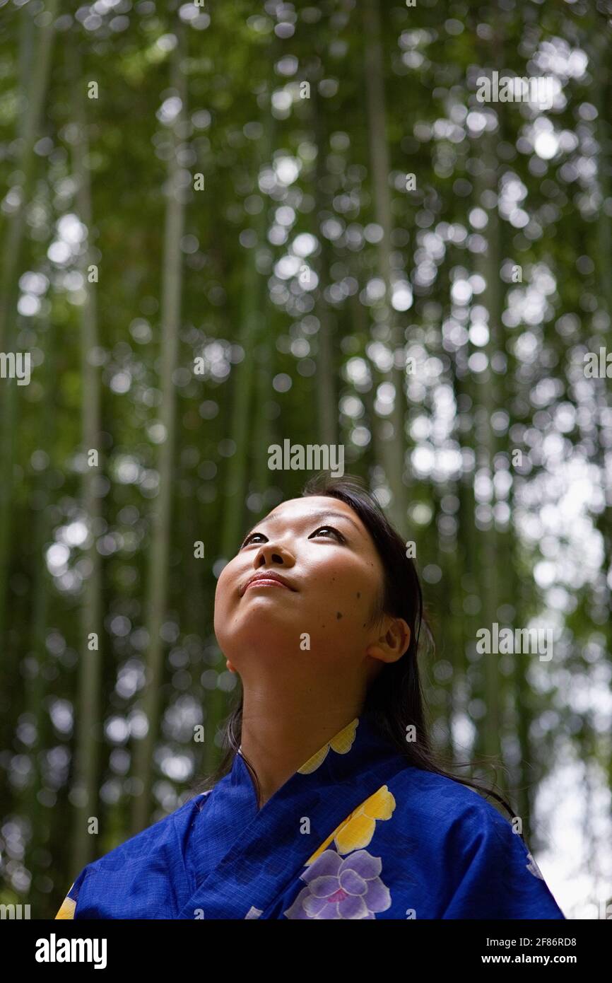 Donna giovane premurosa in kimono guardando su alberi di bambù Foto Stock