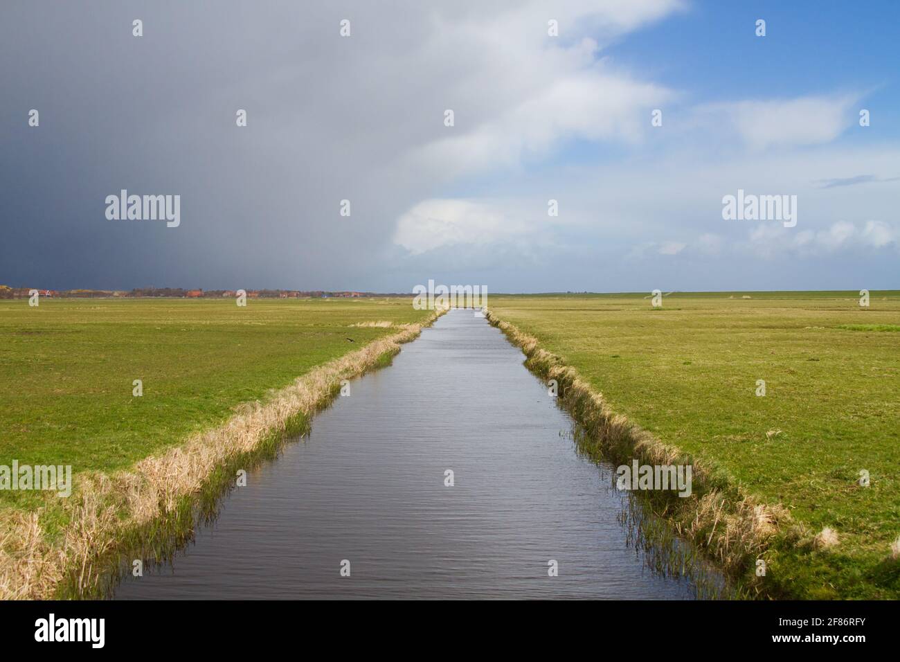 Fronte tempesta che si avvicina sul paesaggio rurale sull'isola olandese Terschelling: Nuvole scure minacciose sopra un paesaggio piano polder con un canale Foto Stock