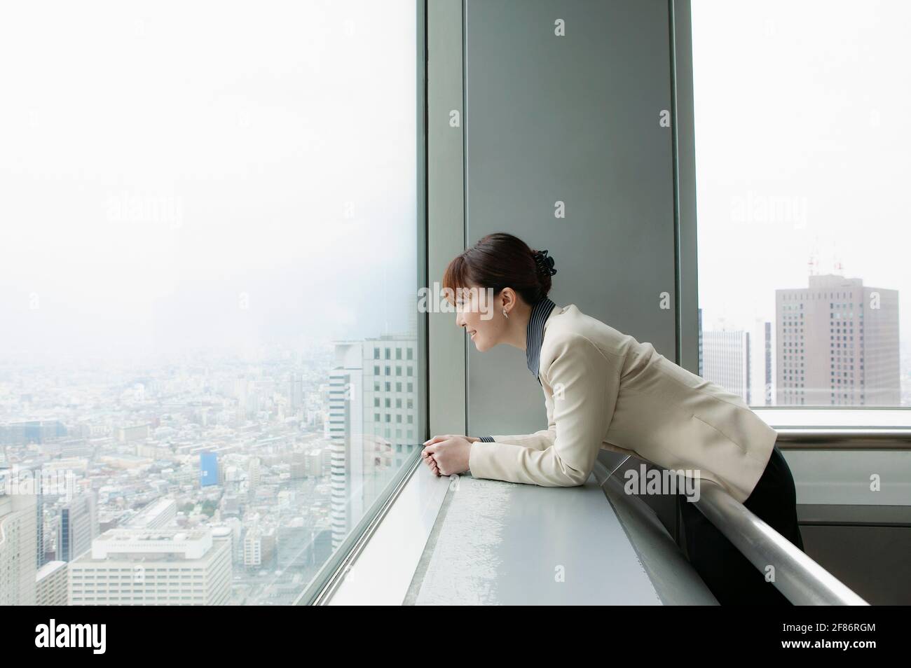 Donna d'affari che guarda fuori dalla città dall'alto ufficio Foto Stock