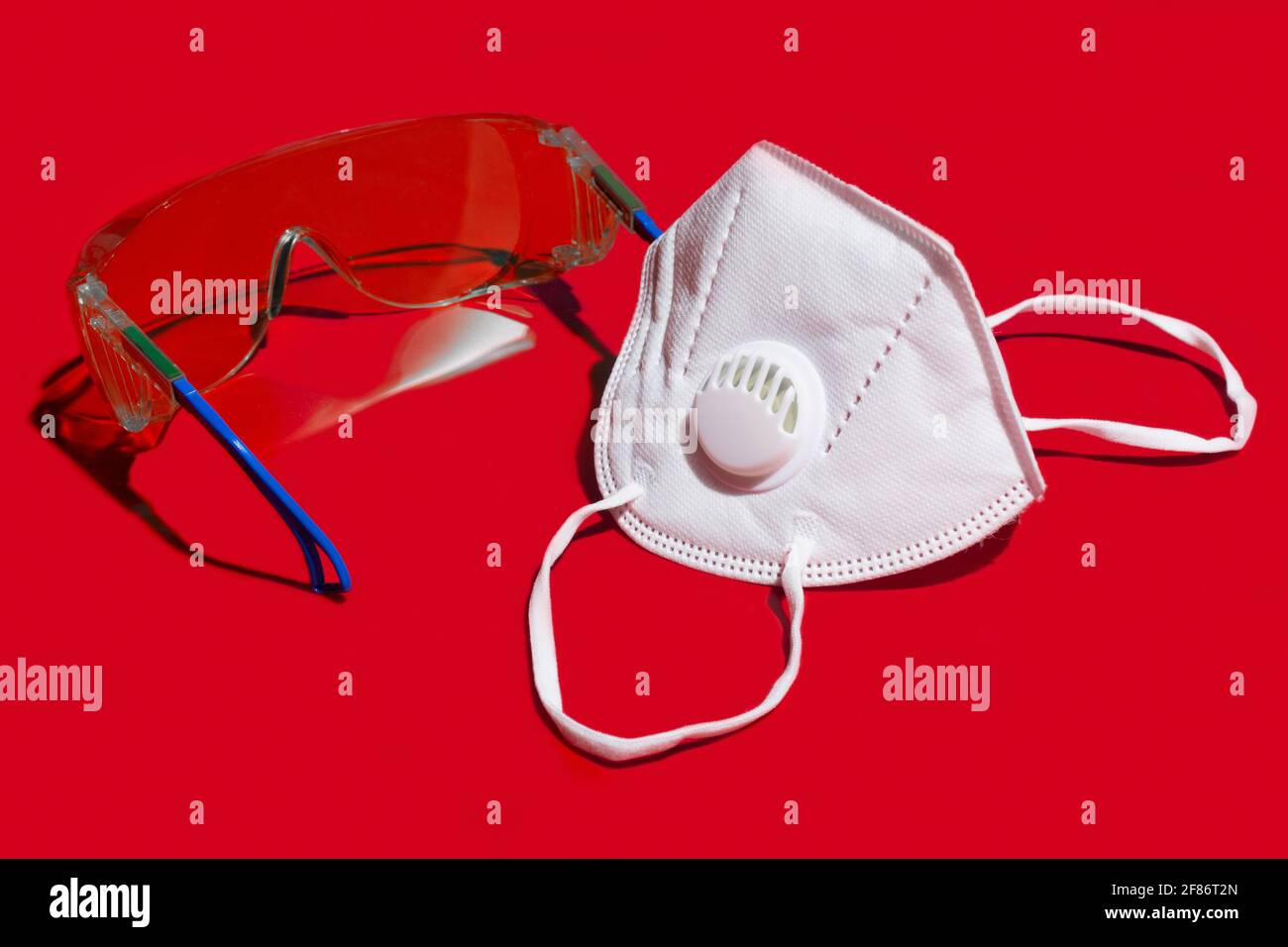 Primo piano maschera facciale N95 e occhiali di protezione sul colore rosso sfondo Foto Stock