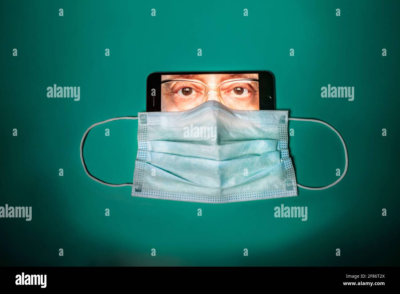 Maschera facciale che copre il volto dell'uomo sullo schermo dello smartphone Foto Stock