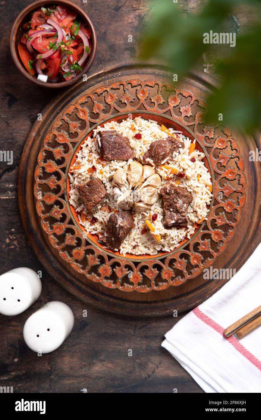 Il concetto di cucina orientale. Piatto asiatico tradizionale - pilaf di riso, verdure e carne in un piatto su un tavolo di legno. Immagine di sfondo. Top vie Foto Stock