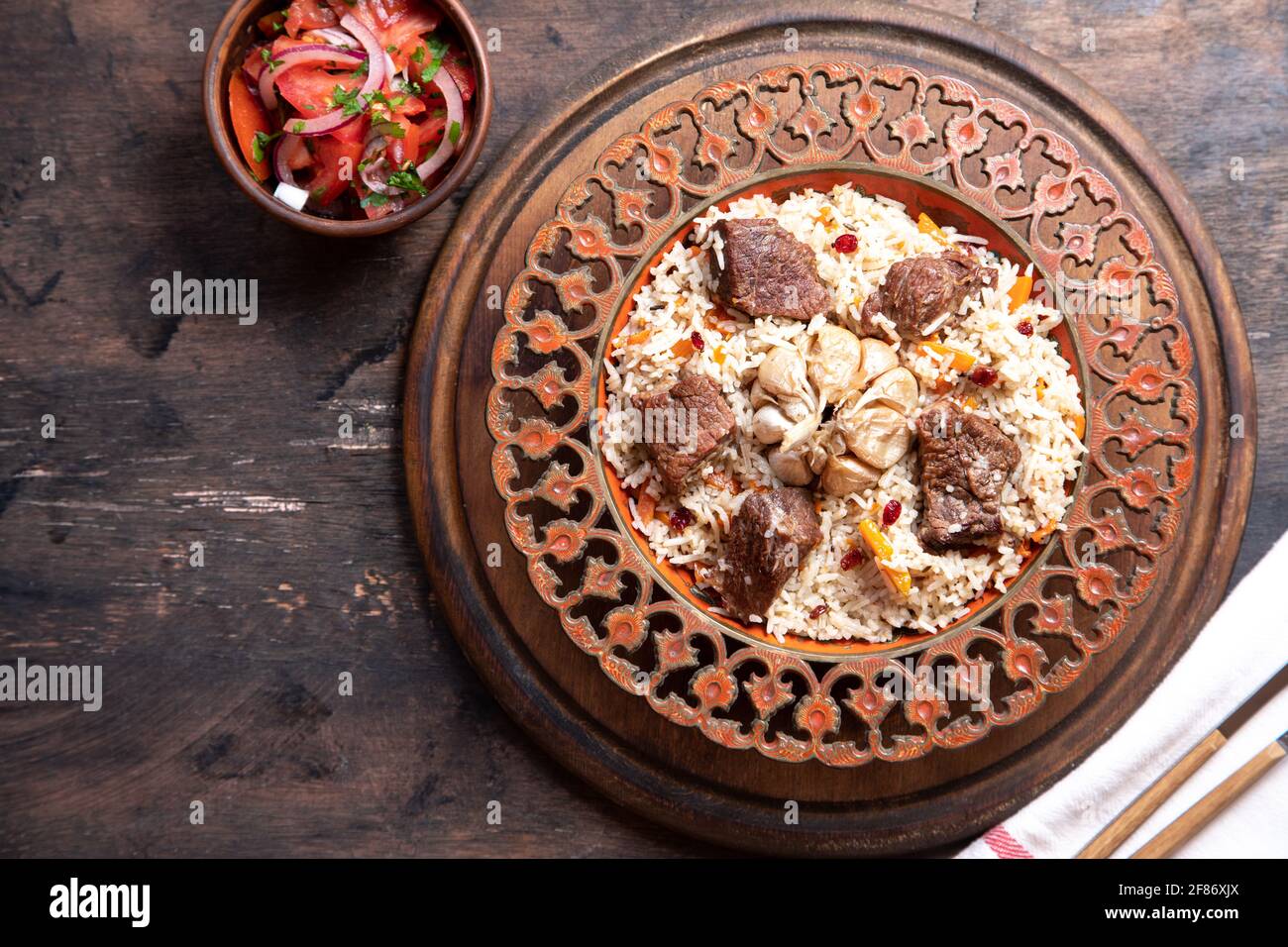 Il concetto di cucina orientale. Piatto asiatico tradizionale - pilaf di riso, verdure e carne in un piatto su un tavolo di legno. Immagine di sfondo. Top vie Foto Stock