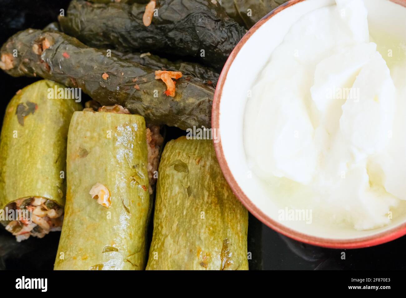 Zucchine farcite con carne tritata e riso. Presentazione di foglie ripiene (sarma yaprak) con yogurt, coltello, forchetta e cucchiaio su sfondo bianco. Foto Stock