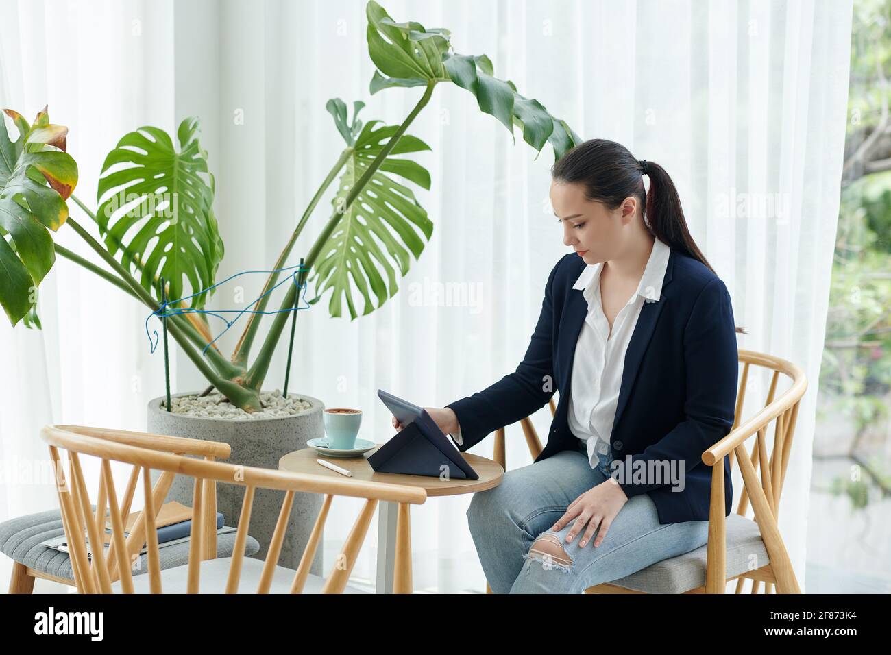 Bella giovane imprenditore femminile seduto al tavolo del caffè e la lettura articolo sul computer tablet Foto Stock
