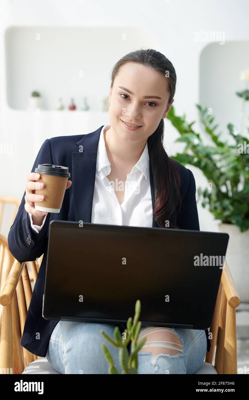 Sorridente prety univeristy studente che beve caffè e lavora su un computer portatile in caffetteria Foto Stock