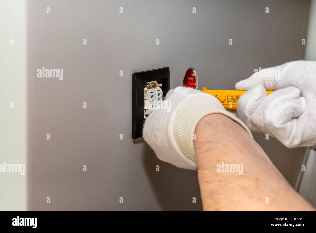 L'elettricista avvita gli otturatori a rullo verso l'alto e verso il basso con un cacciavite giallo nella stanza accanto alla finestra. Foto Stock