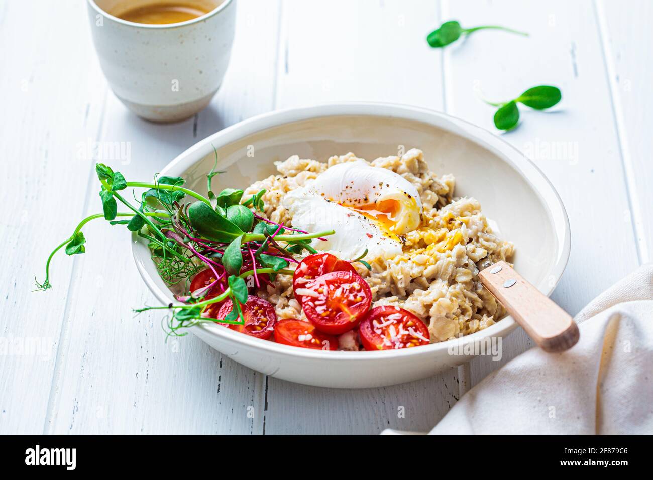 Farinata d'avena saporita con uova in camicia, pomodori, formaggio e germogli in un recipiente bianco. Concetto di colazione salutare. Foto Stock