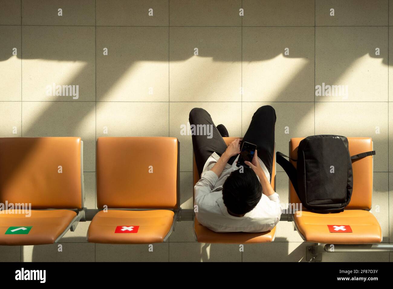 passeggero asiatico uomo d'affari che indossa una maschera lavorando sul telefono cellulare e. siediti sulla sedia di distanza sociale mentre aspetti il volo a. terminal dell'aeroporto durin Foto Stock