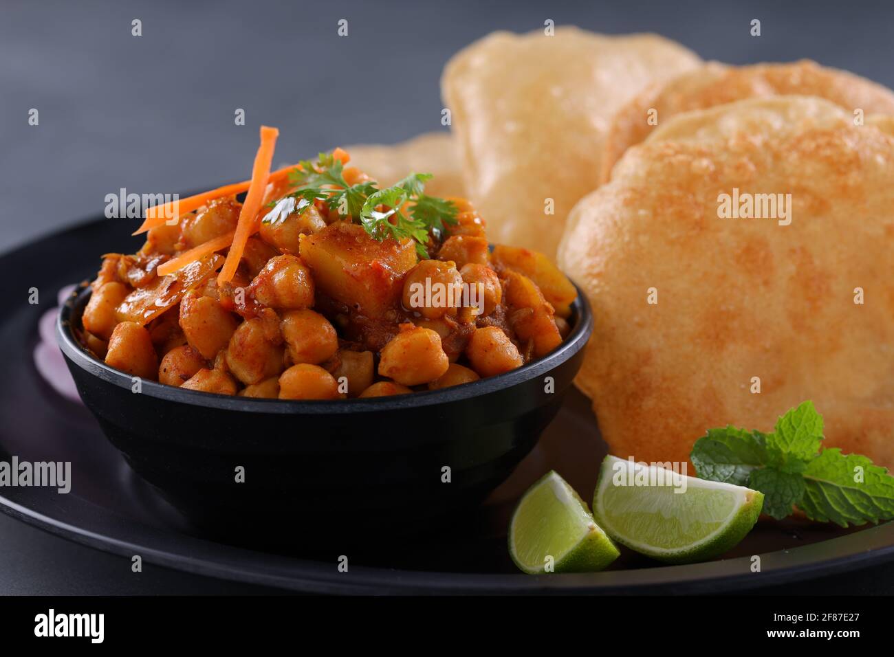 Colazione indiana  Poori con ceci chana masala curry, gustoso piatto indiano fatto usando farina di grano di tutti gli scopi che è disposto in una piastra nera con Foto Stock