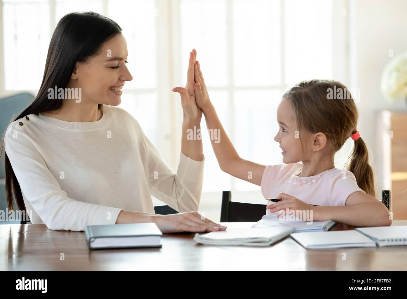 Felice mamma e piccola figlia finitura compiti dare alto cinque Foto Stock