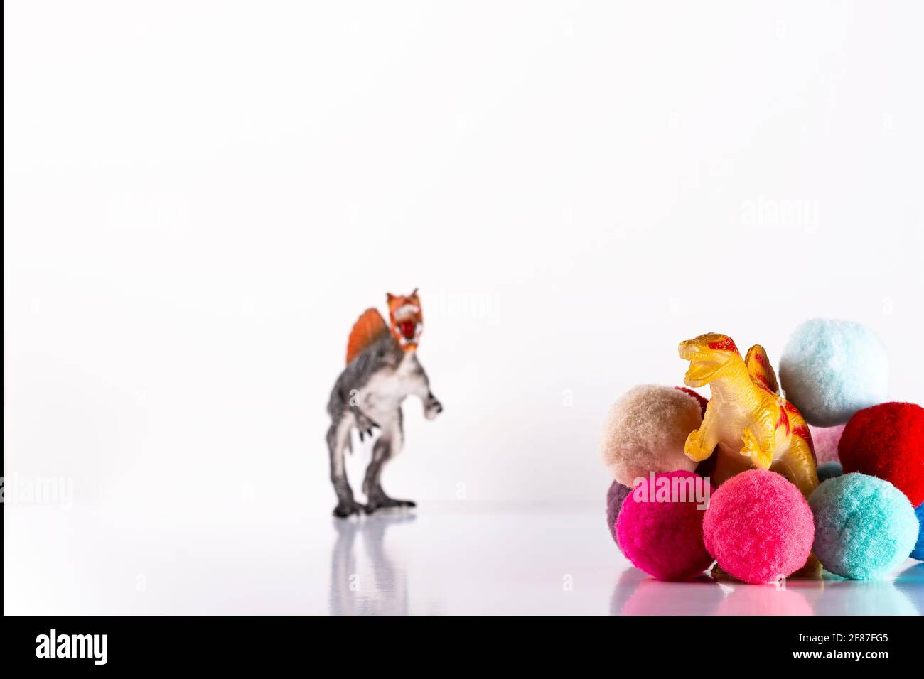 Dinosauro giocattolo che emerge da palle di spugna colorate e da un dinosauro Fuori fuoco nello sfondo. La fotografia è orizzontale girato su uno sfondo bianco Foto Stock