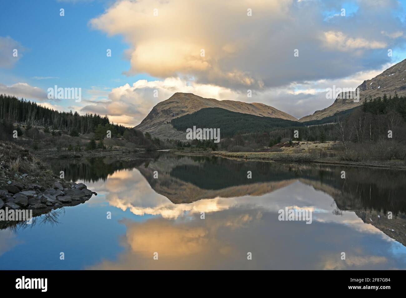 Paesaggio tramonto di Argyll e Bute, Scozia con le nuvole riflesse in piccolo lochan, montagne e foresta sullo sfondo. Foto Stock