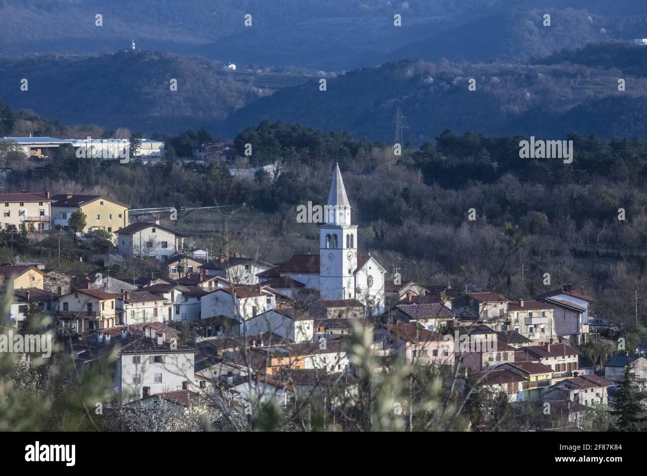 Tardo Afternon Tiro di Villaggio di Osek nella Valle di Vipava Slovenia. Situato nel mezzo della Valle. Surrogato da colline e zona coltivata. Molti Mon sacrale Foto Stock