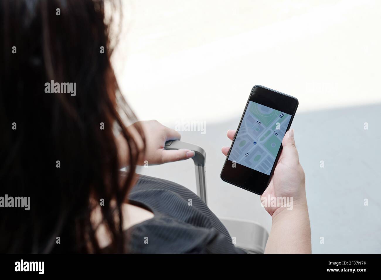 Donna che controlla l'applicazione sullo smartphone in attesa di taxi auto per l'aeroporto Foto Stock