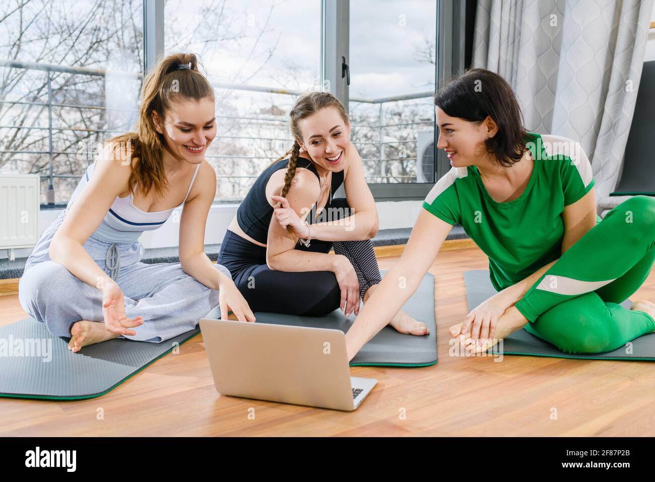 Tre ragazze sportive si siedono sui tappetini in palestra durante esercitazioni in linea di addestramento di esercitazione di yoga Foto Stock