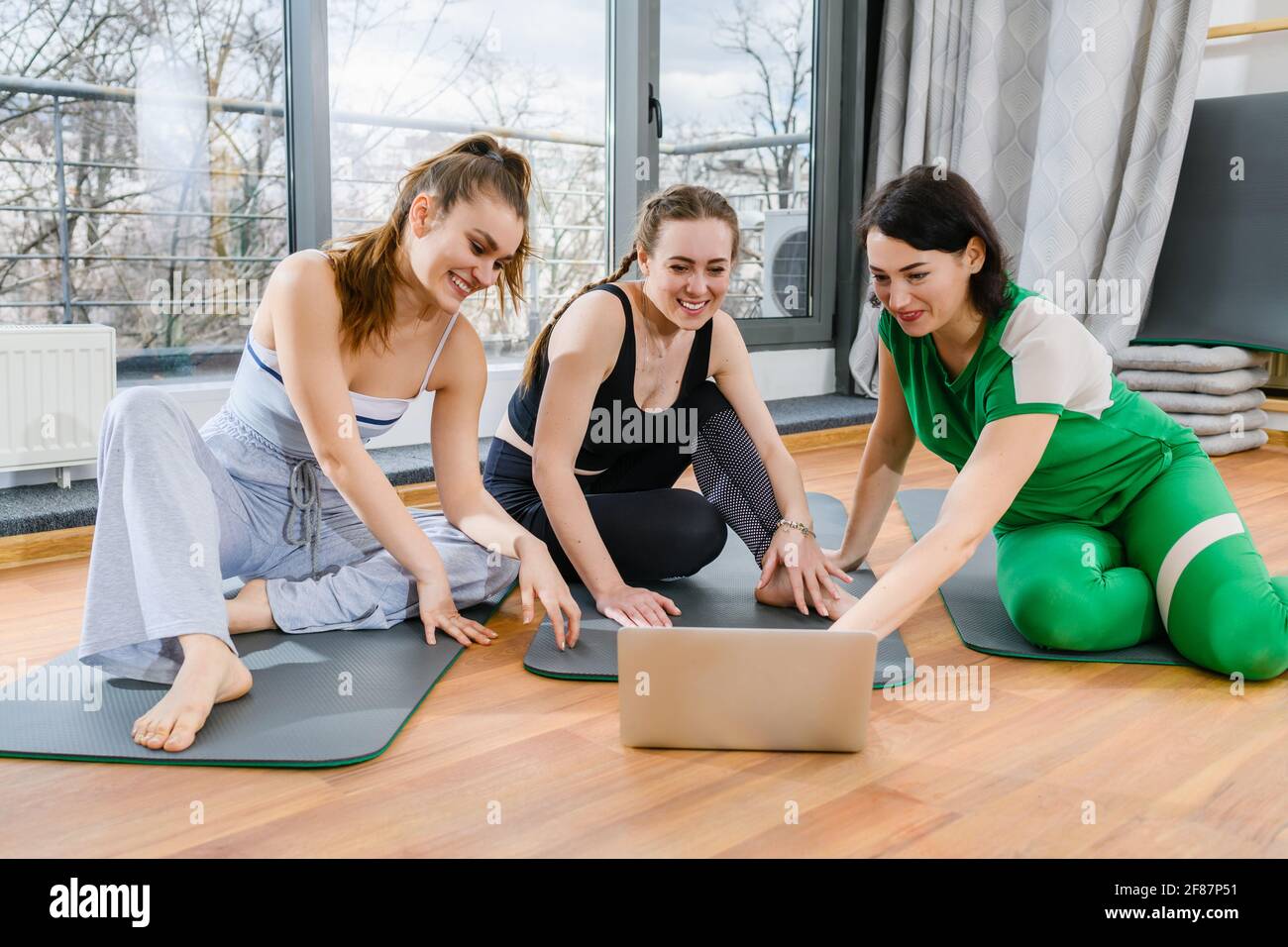 Tre ragazze sportive si siedono sui tappetini in palestra durante esercitazioni in linea di addestramento di esercitazione di yoga Foto Stock