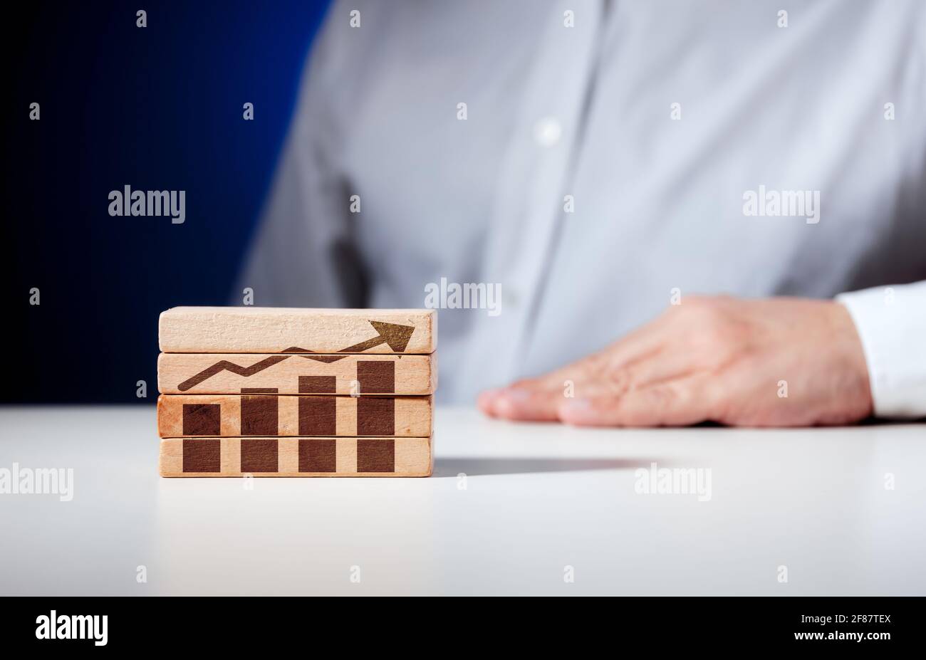 Un grafico di affari con tendenza di crescita scolpita su blocchi di legno con un uomo d'affari seduto sullo sfondo. Crescita economica o finanziaria, progresso e pr Foto Stock