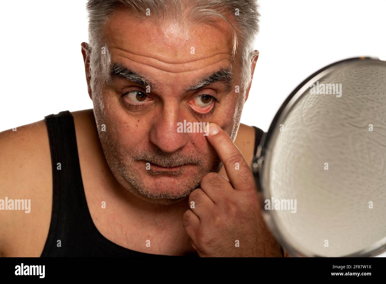 l'uomo medio invecchiato che gli palpava la palpebra inferiore su sfondo bianco Foto Stock