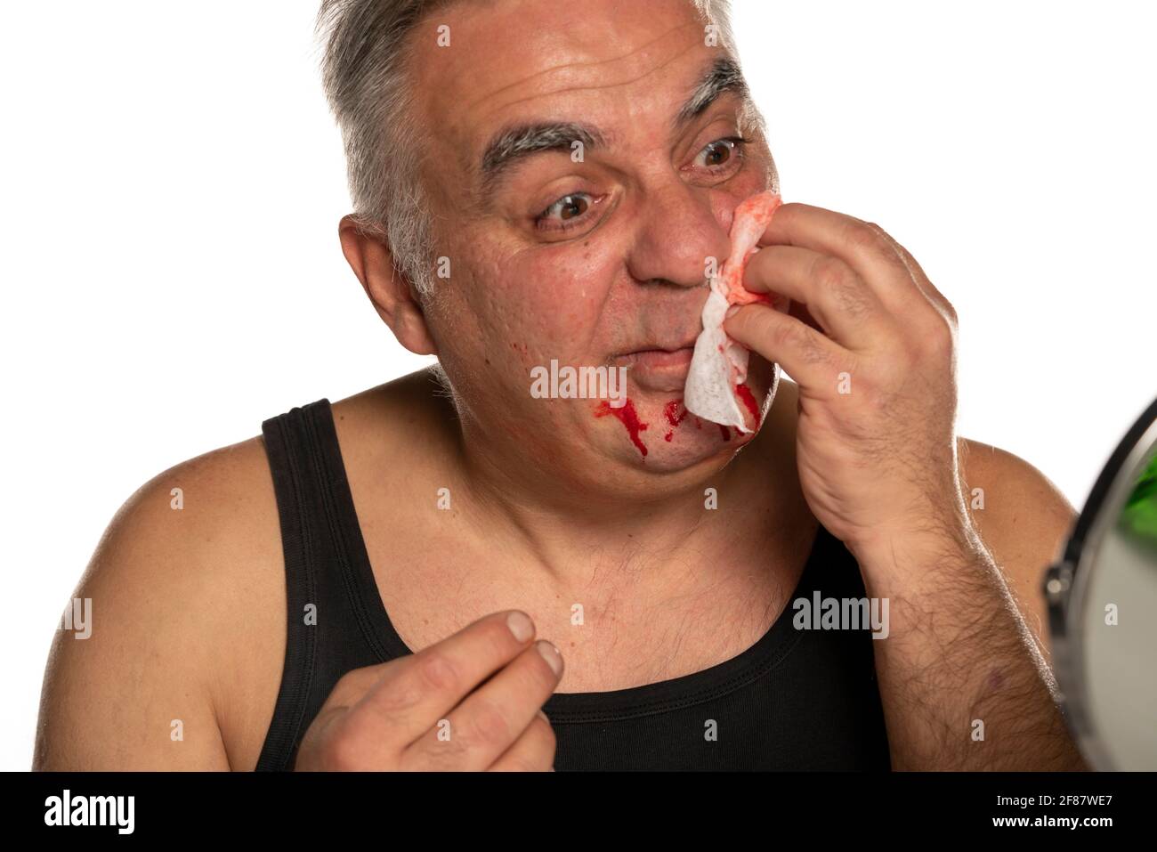 nervosa uomo di mezza età che pulisce sangue dal viso con tessuto su sfondo bianco Foto Stock