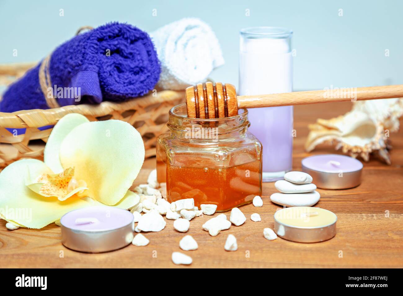 Trattamento benessere al miele. Vaso miele dorato, fiori di orchidee, asciugamani e candele aromatiche. Cura naturale della pelle domestica. Foto Stock