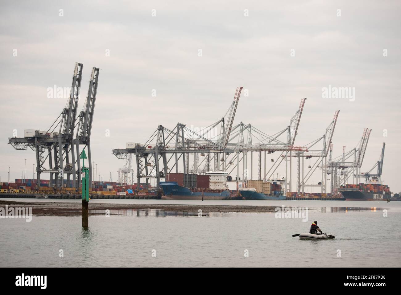 Southampton ormeggia con l'uomo in dingy remando lungo in primo piano Acqua con dock del deposito DP sullo sfondo Foto Stock