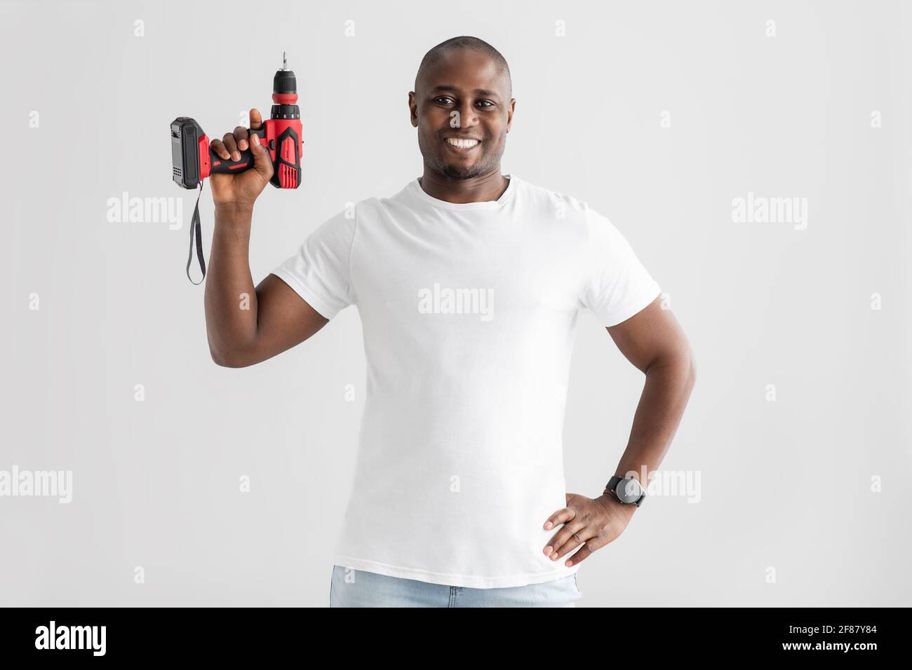 Strumenti di ristrutturazione. Felice uomo afro-americano che tiene trapano elettrico, isolato su sfondo bianco Foto Stock