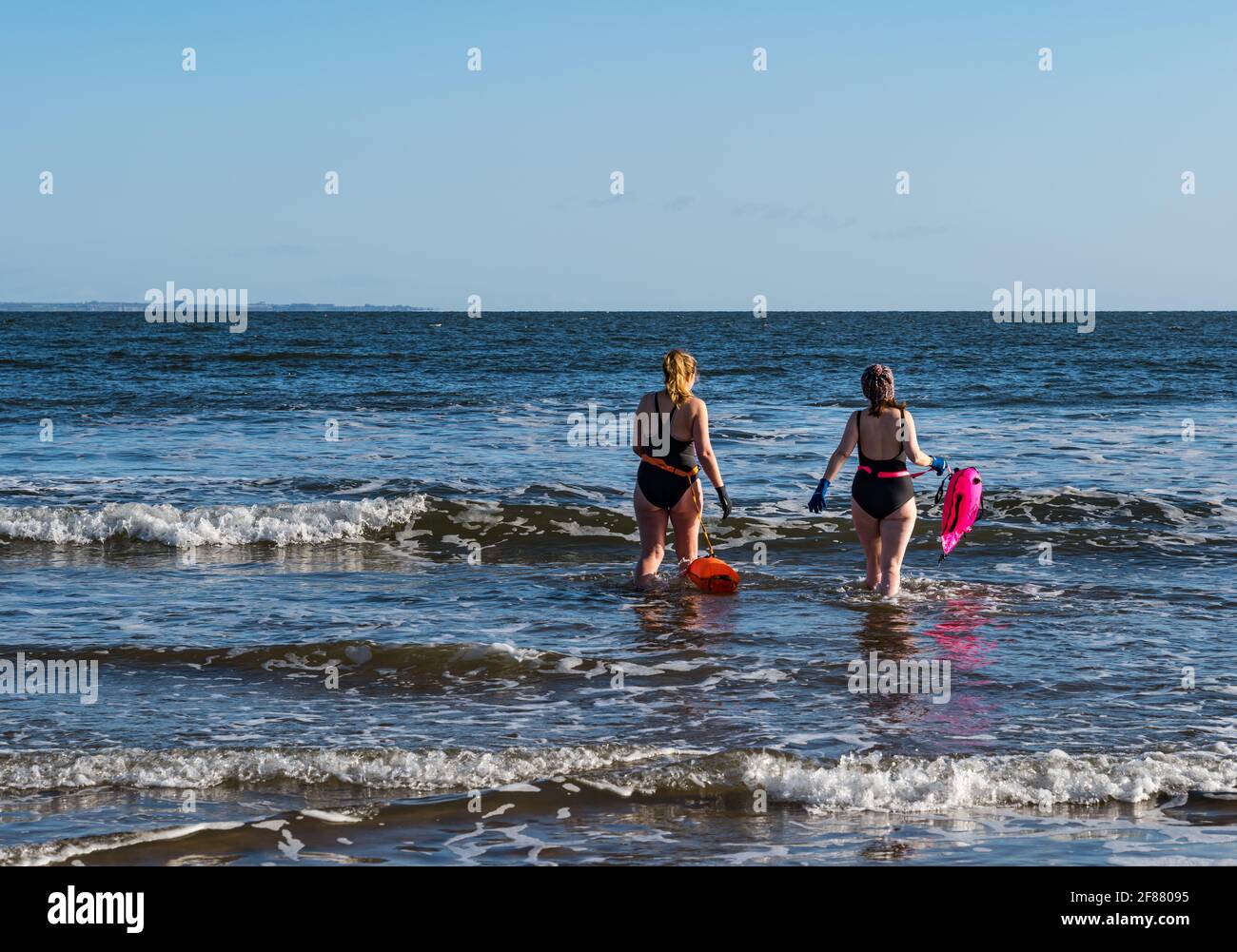 Due donne nuotatori selvatici o in mare aperto in costume da bagno con galleggianti vanno in mare in una giornata di sole, Firth of Forth, Scozia, Regno Unito Foto Stock