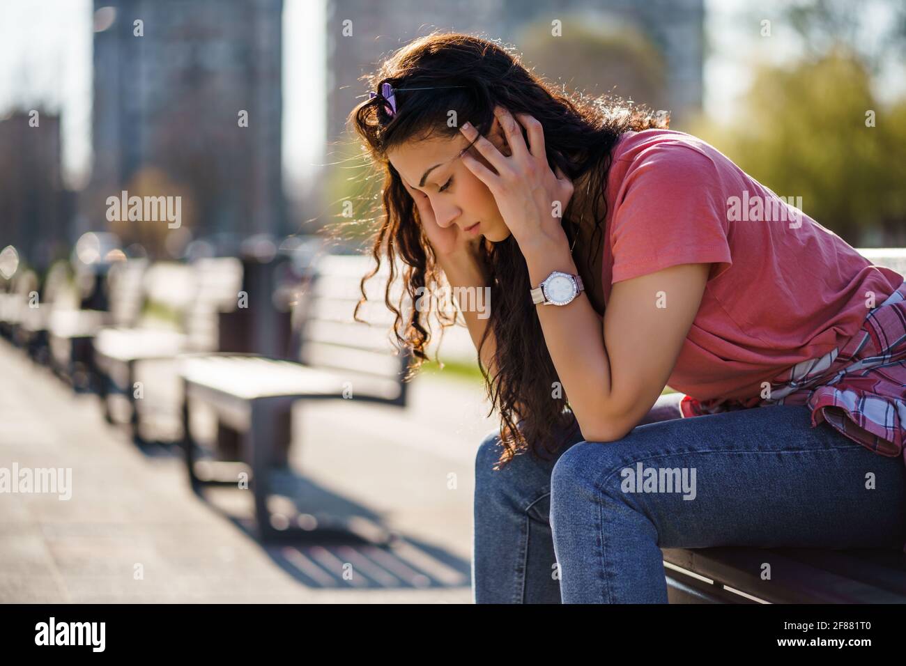 Triste giovane donna è seduta su panchina in città. È depressa. Foto Stock