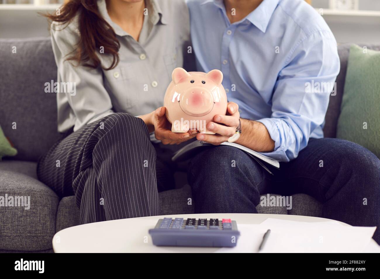 Immagine ritagliata di una banca piggy nelle mani di una giovane famiglia che pianifica il loro bilancio. Foto Stock