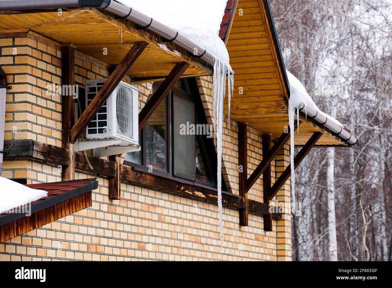 Grandi icicles appendono sotto il tetto di una casa privata. Caduta della molla. Foto Stock