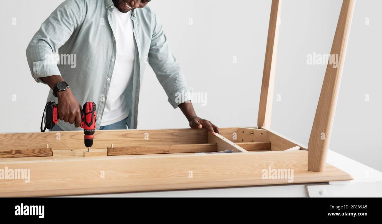 Esperto artigiano che fora tavole di legno di tavola, assemblando mobili con trapano elettrico, panorama Foto Stock